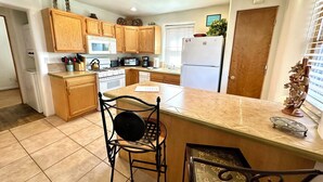 A kitchen with wooden cabinets, a central island, a stove, a microwave, and a refrigerator. - Casita D - 2 Bed, 2 Bath (Single Level) (Santa Fe)
