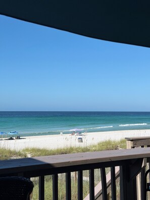 A beach view from a balcony with a wooden railing, a sandy beach, and the ocean.