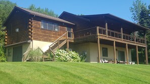 A two-story log cabin with a balcony, surrounded by a well-maintained lawn and trees. - Overlook Cabin: E. Bluff Drive, Lake View, Hot Tub, Firepit, Central-AC, Private (Penn Yan)