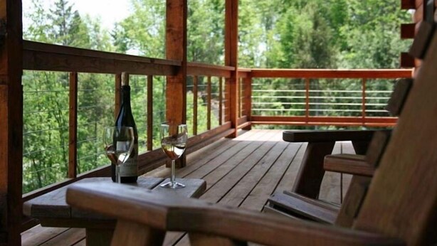 A wooden deck with a table and chairs, overlooking a forested area. - Overlook Cabin: E. Bluff Drive, Lake View, Hot Tub, Firepit, Central-AC, Private (Penn Yan)