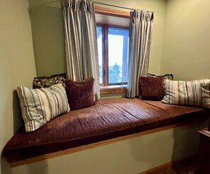 A cozy room with a built-in bench seat, a window with curtains, and a view of trees outside.