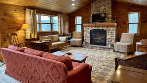 A cozy cabin interior with a stone fireplace, wooden walls, and a ceiling fan. - Overlook Cabin: E. Bluff Drive, Lake View, Hot Tub, Firepit, Central-AC, Private (Penn Yan)