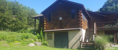 A wooden cabin with a green door, a small porch, and a staircase leading to an upper level.
