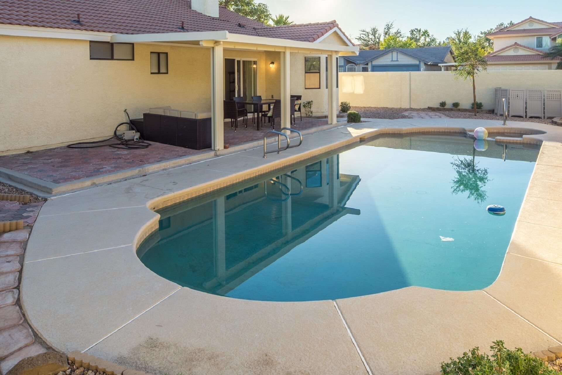 A swimming pool with a curved edge, a covered patio area with outdoor furniture, and a clear sky.