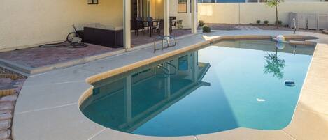 A swimming pool with a curved edge, a covered patio area with outdoor furniture, and a clear sky.