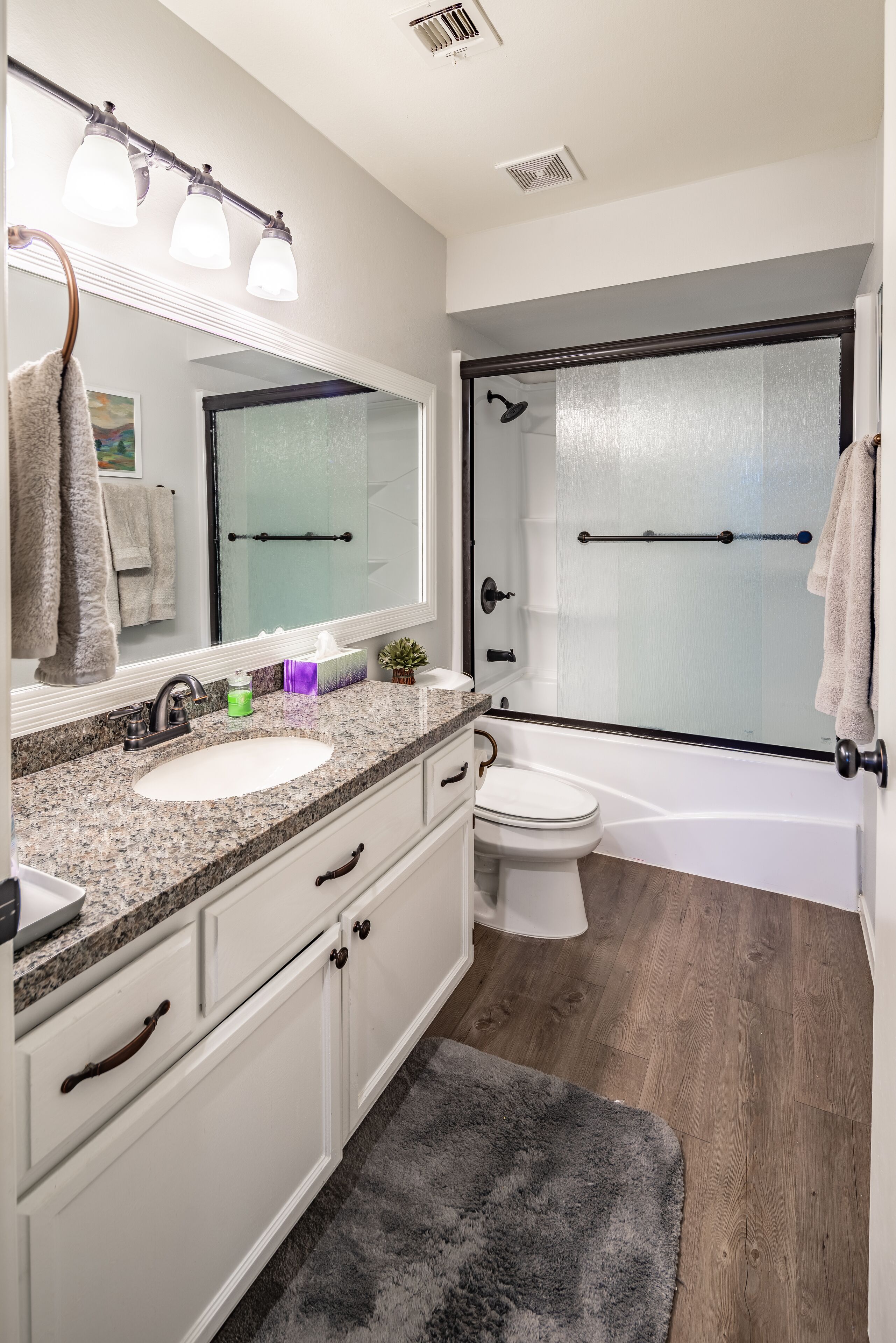 A modern bathroom with a granite countertop sink, a white toilet, and a glass-enclosed shower.