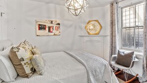 A bedroom with a bed, a chair, a wall-mounted picture, and a hanging light fixture.