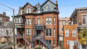 A multi-story brick building with a prominent corner entrance, a fire escape, and a balcony.