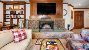 A living room with a stone fireplace, a television mounted above it, and two sofas with plaid cushions.