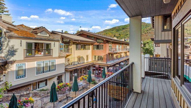 A multi-story building with balconies, outdoor seating areas, and a view of a hilly landscape.