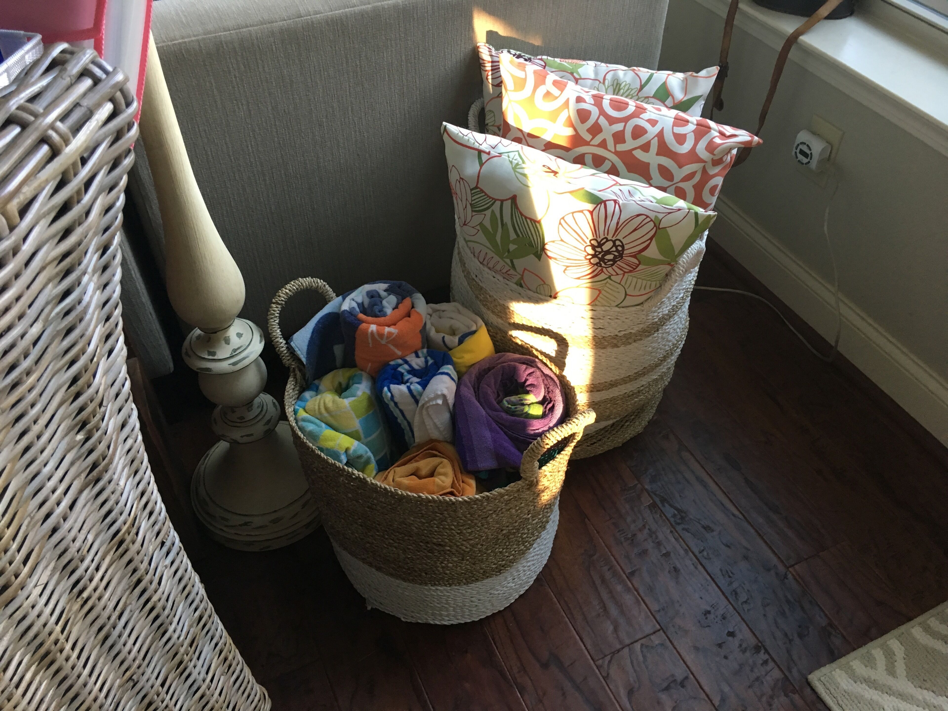 A corner of a room with a wicker basket filled with colorful towels and a woven basket.