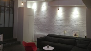 A modern interior with a black sofa, a red chair, and a small table. There is a white brick wall and a skylight above. - QUIET RENOVATED INDUSTRIAL LOFT IN "GRANDS BOULEVARDS" AREA; PARIS THEATRES AREA (Paris)