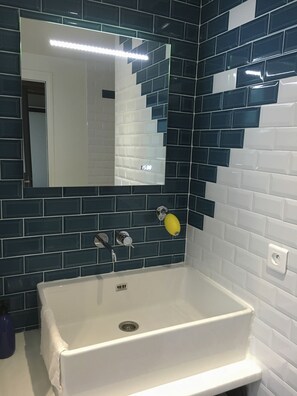 A bathroom with a white sink, a mirror, and a wall with blue and white tiles. - QUIET RENOVATED INDUSTRIAL LOFT IN "GRANDS BOULEVARDS" AREA; PARIS THEATRES AREA (Paris)