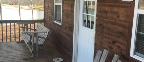 A wooden cabin with a porch, two benches, and a door with a welcome sign.