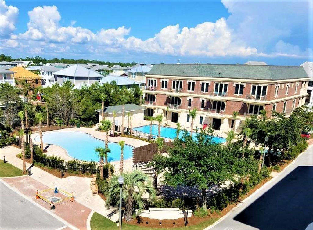 Ein großes Gebäude mit Swimmingpool, umgeben von Grünflächen und anderen Wohnhäusern.
