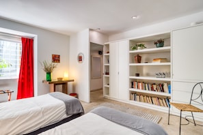 Quarto moderno com duas camas, uma estante, uma escrivaninha e uma cortina vermelha.