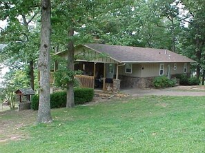 A single-story house with a porch, surrounded by trees and a grassy yard. - Perfect Beaver Lake Access! Firepit, Fishing/Swimming, Convenient to Rogers (Rogers)