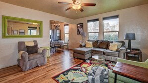 A spacious living room with hardwood floors, a ceiling fan, a large mirror, a dining area with a table and chairs, and a sofa with a colorful rug. - Abba House Downtown  (Prescott)