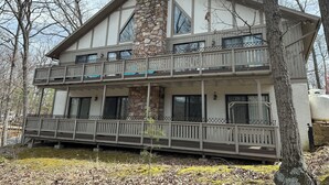 A two-story cabin with a stone chimney, large windows, and a balcony with railings. - Splendid European-Style Chalet w/ Game Room and Renovated Baths (McGaheysville)