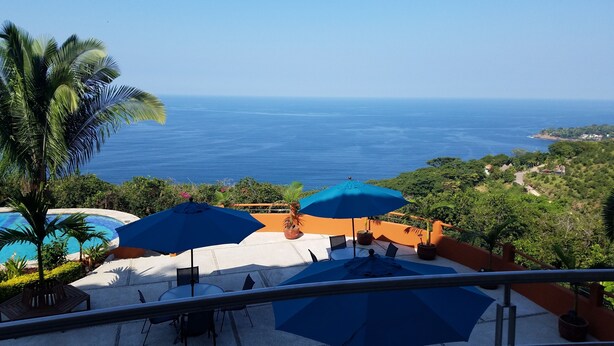 Terraza con mesas al aire libre y sombrillas, con vistas a la costa.
