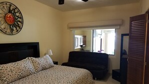 Un dormitorio con cama, ventilador de techo, ventana con cortinas, espejo y puerta.