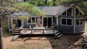 Une cabane dotée d’une terrasse, de meubles de jardin et d’une grande fenêtre donnant sur la forêt environnante.
