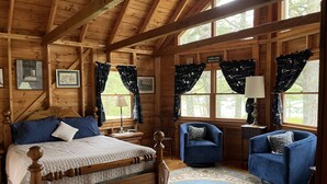 L ’intérieur d’un chalet en bois comprend un lit, deux fauteuils, un tapis et de grandes fenêtres avec des rideaux.