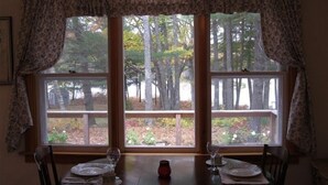 Une table à manger avec deux chaises, une fenêtre donnant sur des arbres et une terrasse, ainsi qu'un vase posé sur la table.