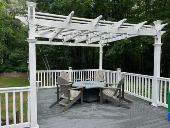 Una terraza cubierta con pérgola, dos sillas Adirondack y una mesa.