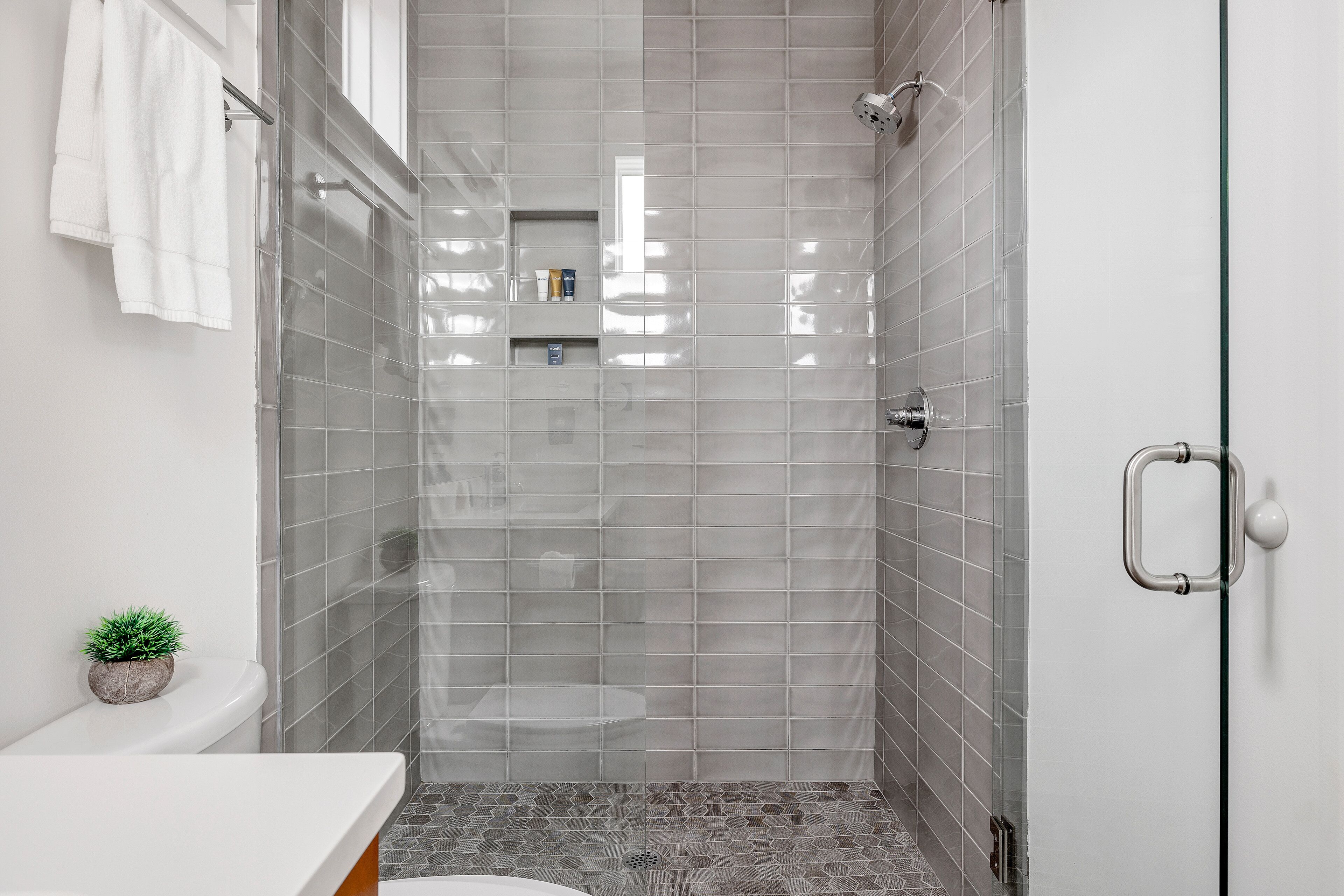 Une salle de bain moderne avec une douche à parois de verre, des carreaux blancs et une petite plante en pot.