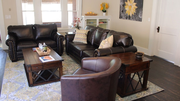 A living room with a black leather sofa, a matching armchair, and a wooden coffee table. There is a bookshelf with books and a vase with flowers. - Casa Rustica - Centrally located, Carlsbad Caverns (Carlsbad)