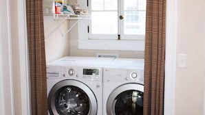 A laundry area with two front-loading washing machines, a window above, and a shelf with cleaning supplies. - Casa Rustica - Centrally located, Carlsbad Caverns (Carlsbad)