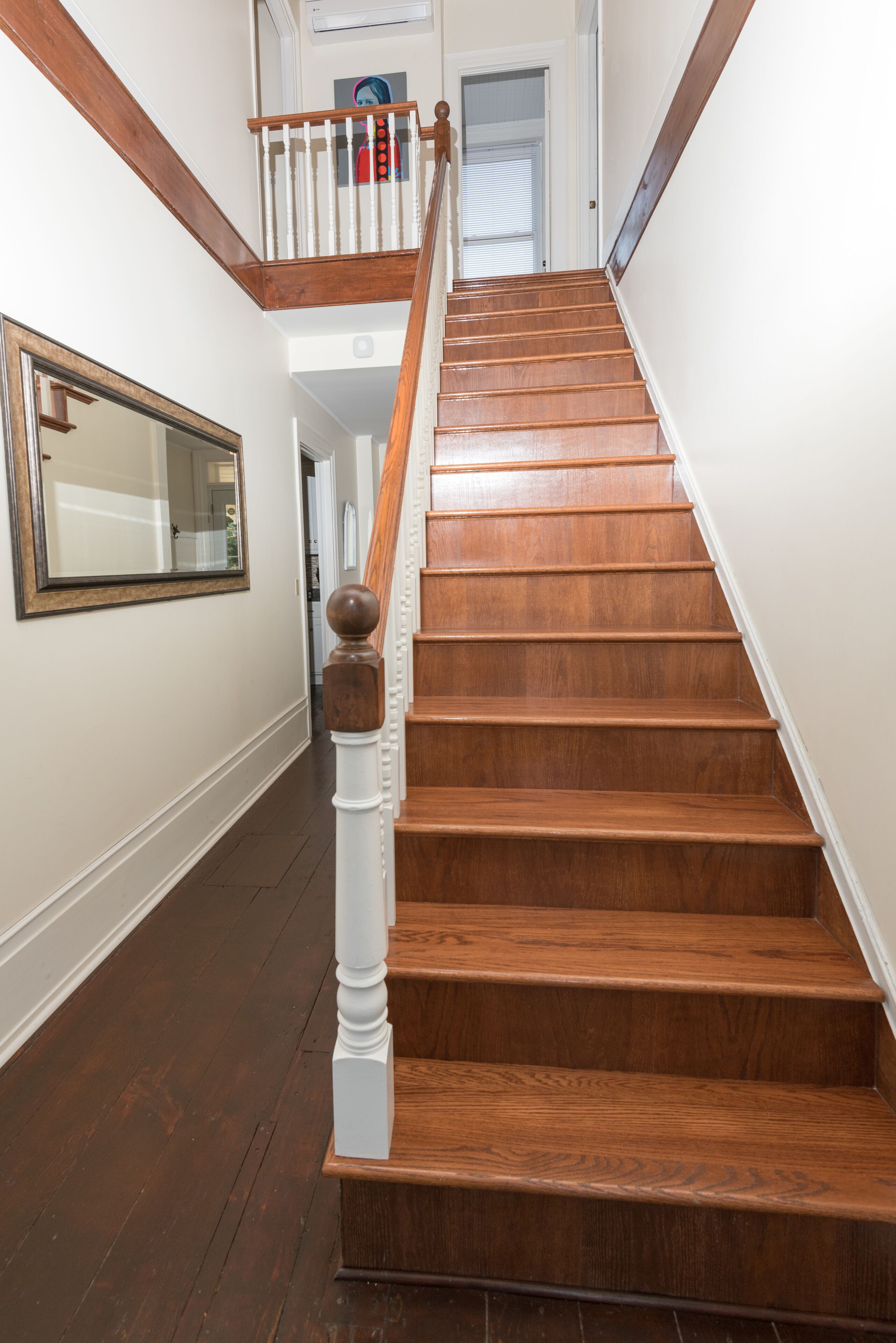 A wooden staircase with white balusters and a handrail, leading to an upper floor.