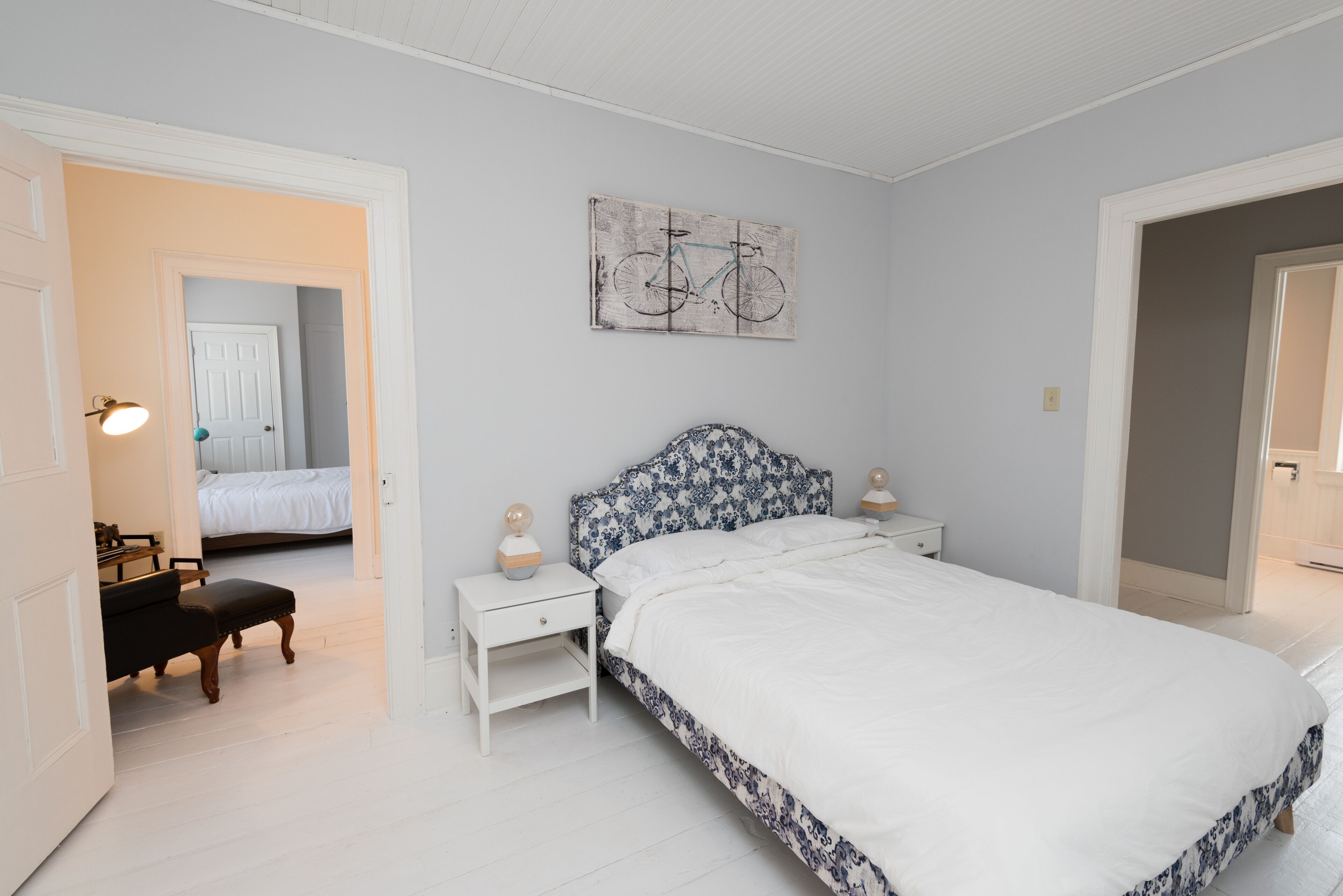 Un dormitorio con cama, una mesita de noche, un banco y una obra de arte con una bicicleta colgada en la pared.
