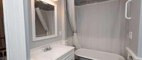 Un baño con una bañera blanca, un lavabo con espejo y una cortina de ducha.
