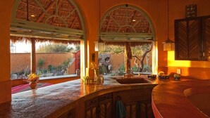A kitchen with a curved countertop, a sink, and a window with a view of a garden. - El Encanto - Artful Luxury in a Rustic Setting by the Sea (Cabo Pulmo)