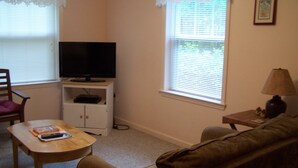 Una sala de estar con televisor sobre un mueble bajo, un sofá, una mesita y una silla.