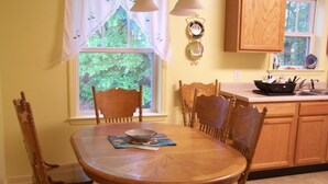 Un comedor con una mesa de madera, cuatro sillas, una ventana con cortinas y una cocina al fondo.