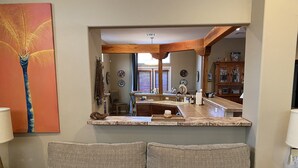 Un salon avec un canapé, deux coussins à motifs, un coin cuisine comprenant un évier et des placards, et un grand miroir qui reflète l’espace.