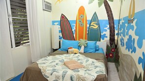 Ein Schlafzimmer mit einem Bett, einem Fenster mit Jalousien und einer Wand, die mit Surfbrettern und einer Palme verziert ist.