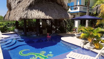 A swimming pool with a thatched roof structure, lounge chairs, and a decorative tile pattern.