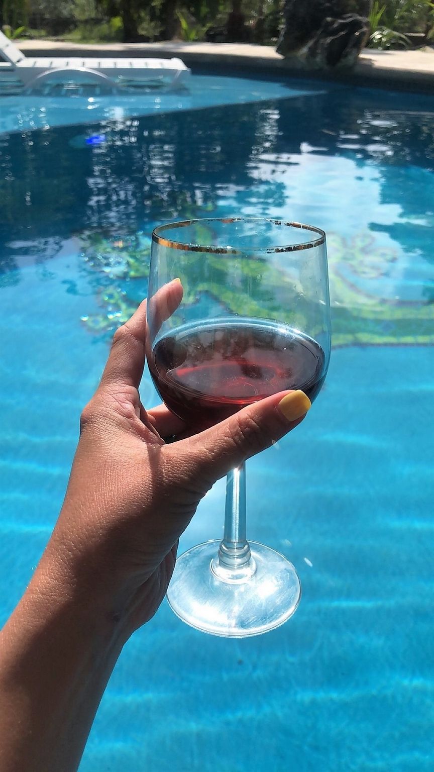 A hand holding a wine glass over a swimming pool.