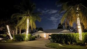 A residential area at night with illuminated palm trees, a driveway, and a house with a covered porch. - Hot Tub, Salt Air & Sunsets Your Naples Beach Retreat (Naples)