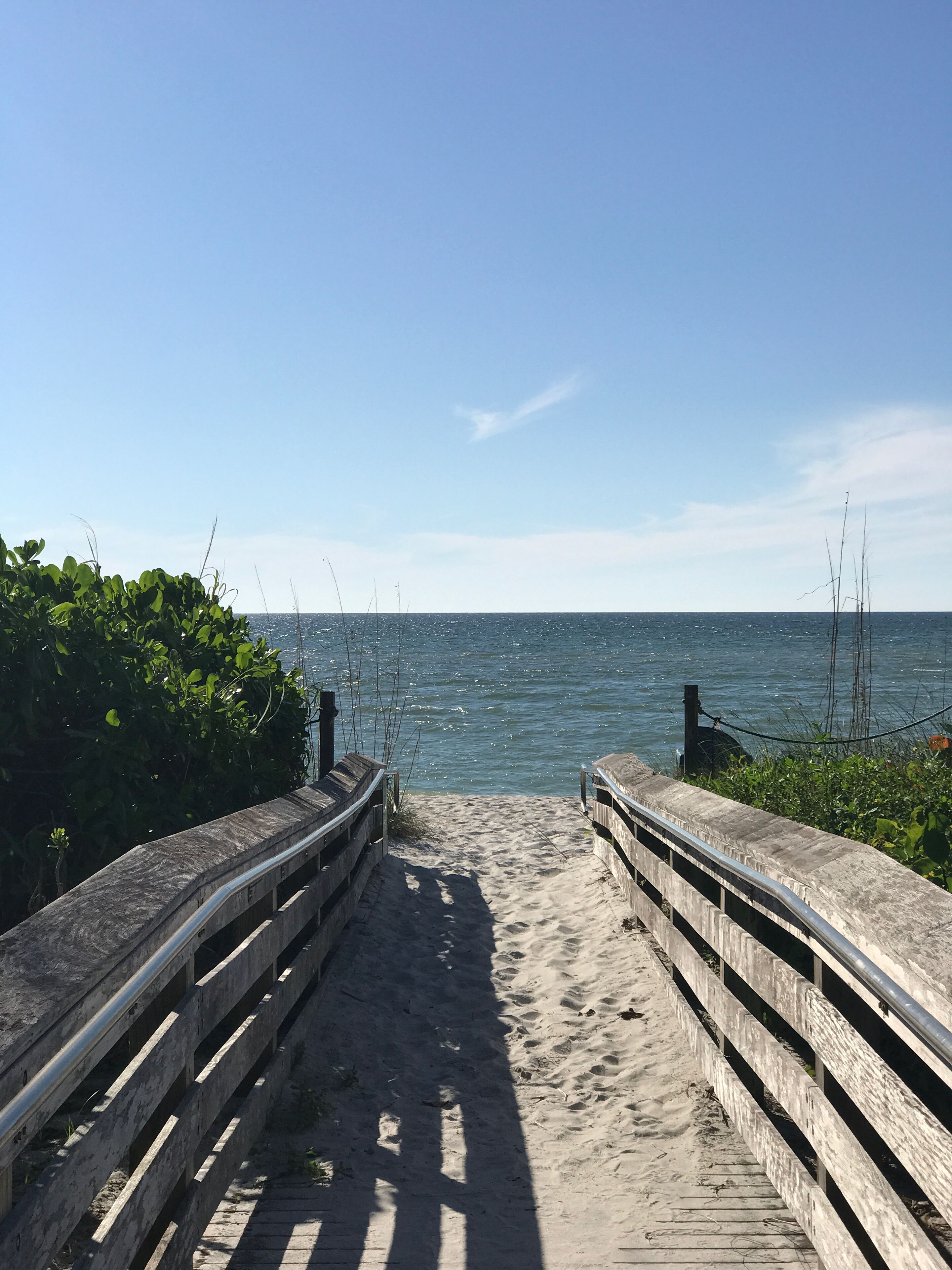 A wooden boardwalk leading to a sandy beach with a clear view of the ocean.