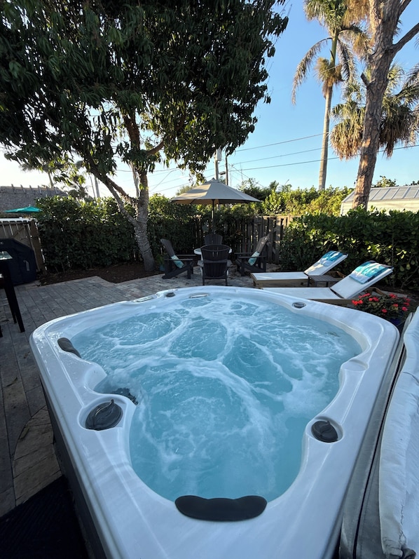 A hot tub with a wooden deck, surrounded by lush greenery and a wooden fence.