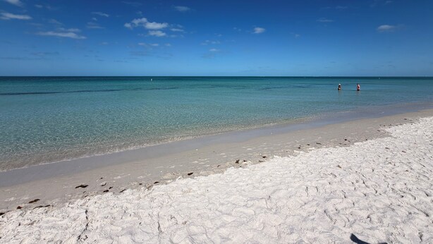 A beach with clear water, a sandy shore, and two people in the distance. - Hot Tub, Salt Air & Sunsets Your Naples Beach Retreat (Naples)