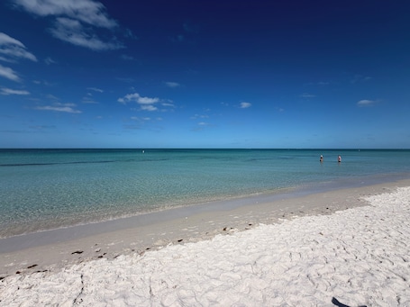 A beach with clear water, a sandy shore, and two people in the distance.. Hot Tub, Salt Air & Sunsets Your Naples Beach Retreat