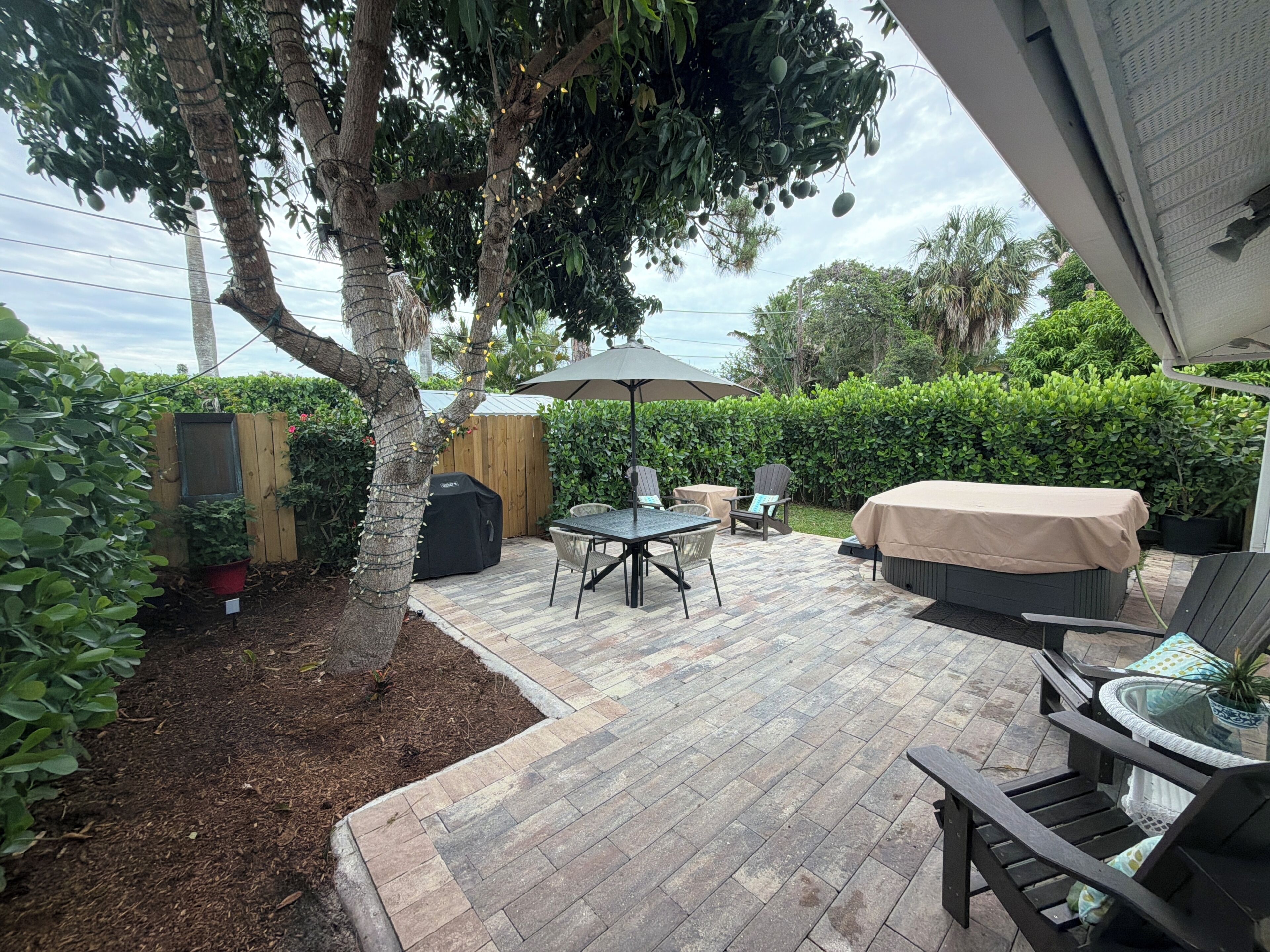 Un espace extérieur aménagé avec une table, des chaises, un barbecue et un coin salon abrité.
