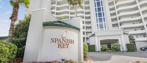 Entrada del hotel Spanish Key con un letrero, palmeras y un edificio de varios pisos.