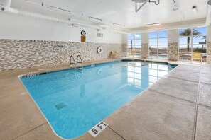 Una piscina interna con acqua limpida, pareti piastrellate e vista su palme all'esterno.